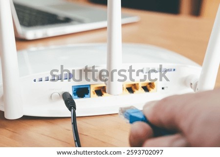 Selective focus at router antenna while men hand connecting fiber cable plug into socket with blurred computer laptop at the background. High speed broadband internet technology at home concept.