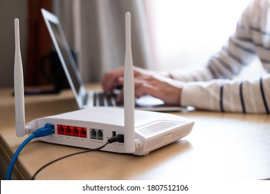 Selective focus at router. Internet router on working table with blurred man connect the cable at the background. Fast and high speed internet connection from fiber line with LAN cable connection. - Shutterstock ID 1807512106
