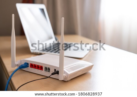 Selective focus at router. Internet router on working table with blurred computer at the background. Fast and high speed internet connection from fiber line with LAN cable connection.