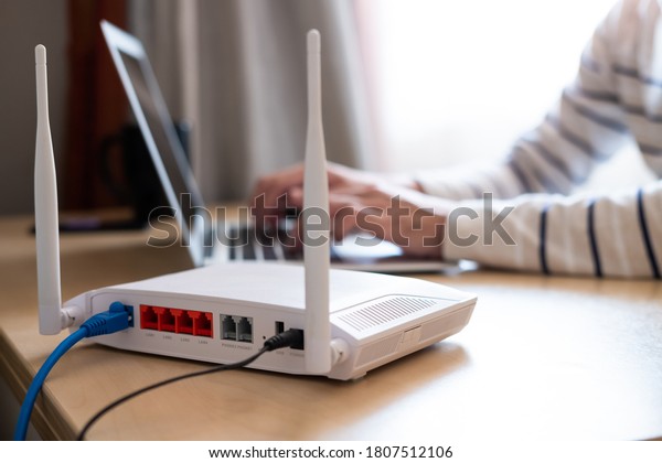 Selective focus at router. Internet router on\
working table with blurred man connect the cable at the background.\
Fast and high speed internet connection from fiber line with LAN\
cable connection.