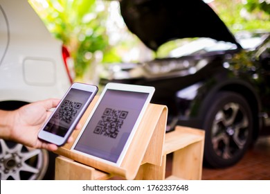 Selective focus to RQ Code on tablet. Blurry hand holding smart phone and scanning qr code to payment on car service center background.