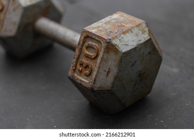 Selective Focus Of Rusted Dumbbell Weight On A Black Gym Floor.