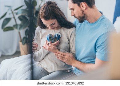 selective focus of sad husband hugging grieving wife with baby shoes