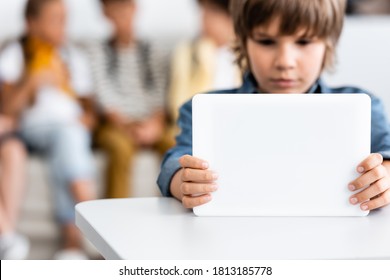 Selective focus of schoolboy using digital tablet at desk in classroom