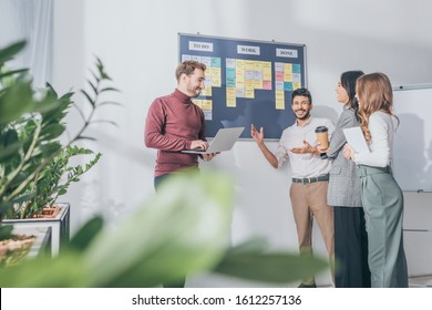 selective focus of scrum master using laptop near board with letters and multicultural coworkers - Shutterstock ID 1612257136