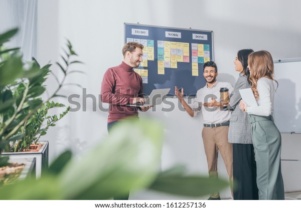 selective focus of scrum master
using laptop near board with letters and multicultural
coworkers