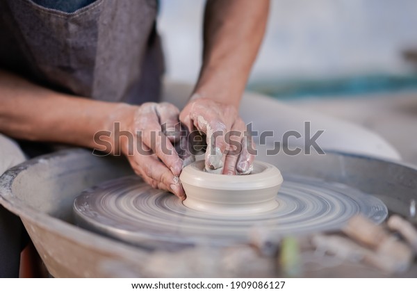 Selective focus sculptor hand
molding clay. Professional artist worker creating a bowl with wet
clay. Image contains certain grain or noise and soft
focus.