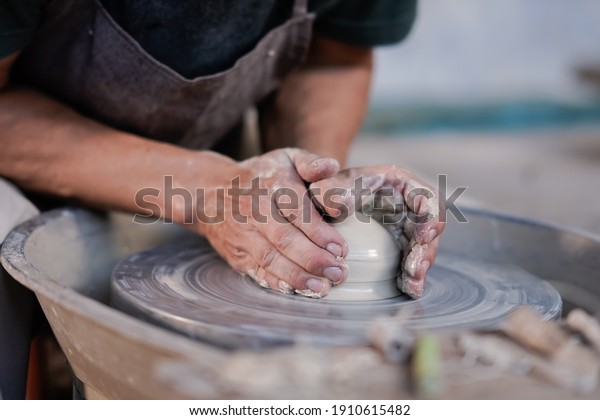 Selective focus sculptor hand\
molding clay. Professional artist worker creating a bowl with wet\
clay. Image contains certain grain or noise and soft\
focus.