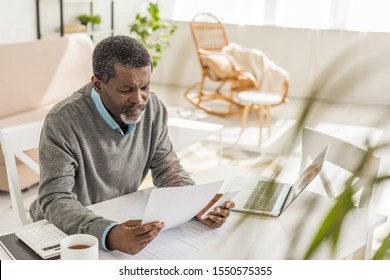 Selective Focus Of Senior African American Man Looking At Utility Bill While Sitting Near Laptop