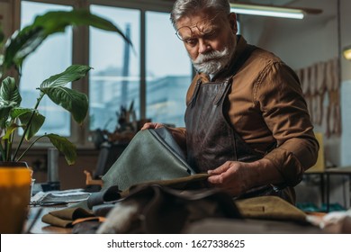 Selective Focus Of Senior Cobbler Holding Pieces Of Genuine Leather In Workshop