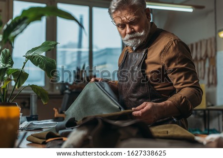 selective focus of senior cobbler holding pieces of genuine leather in workshop