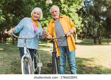 Selective focus of senior couple with smartphone smiling at camera near bikes in park - Powered by Shutterstock