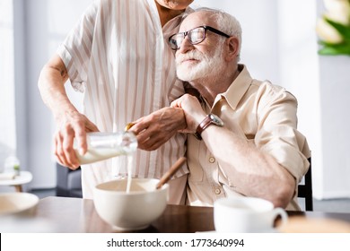 Selective focus of senior man embracing wife pouring milk in bowl during breakfast - Powered by Shutterstock
