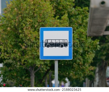 Selective focus shot of a Bus Stop Sign on a metal pole with the tree in the background	
