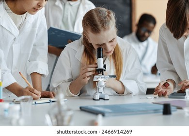 Selective focus shot of Caucasian girl using microscope while doing chemical experiment with classmates during lesson - Powered by Shutterstock