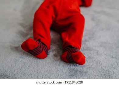 A Selective Focus Shot Of A Newborn Wearing A Red Onesie With Black Stripes On Its Fee