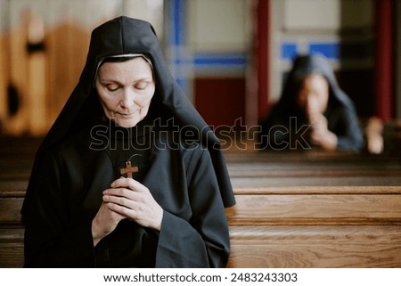 Selective focus shot of pious Catholic nun holding wooden cross in hands praying to Lord, copy space