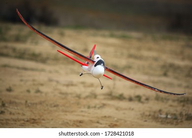 A Selective Focus Shot Of A Red-winged White Flying Model Aircraft With  And A Blurry Field As Background