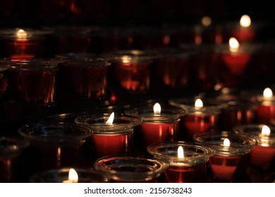 A selective focus shot of row lines of lighted candles arranged in a dark room