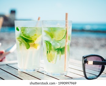 a selective focus shot of two glasses of mojitos and black sunglasses isolated on a table