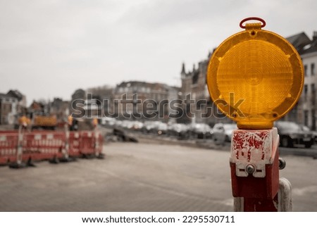 selective focus shot of warning light indicating roadworks and traffic delays due to obstruction in street. Maintenance and construction of road surface means diverted traffic and disruption