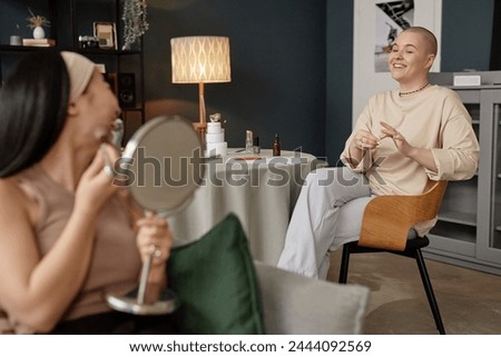 Selective focus shot of young Caucasian woman sitting at table chatting with her Asian friend while removing nail polish