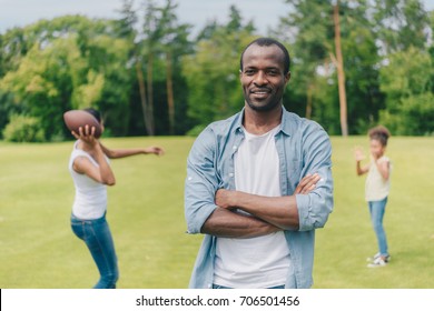 Selective Focus Of Smiling African American Man Looking At Camera While Family Playing American Football Behind