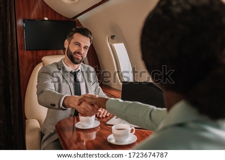 selective focus of smiling businessman shaking hands with african american businesswoman in plane