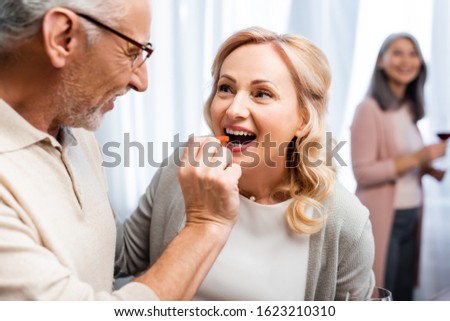selective focus of smiling man giving cut bell pepper to his smiling friend