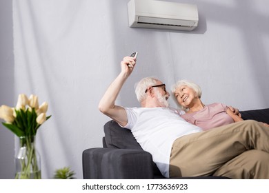 Selective focus of smiling man switching air conditioner with remote controller near wife