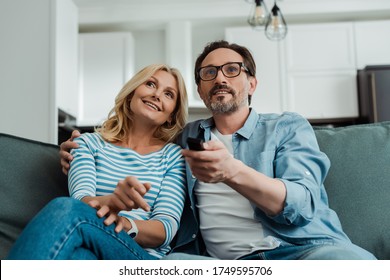 Selective focus of smiling mature couple watching tv on sofa