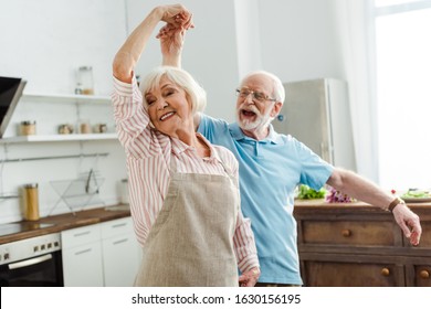 Selective focus of smiling senior couple dancing in kitchen - Powered by Shutterstock