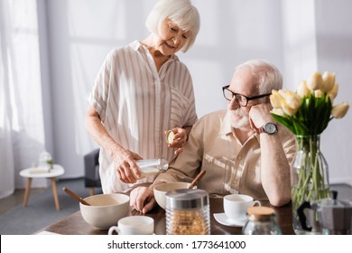 Selective focus of smiling senior woman pouring milk in bowl near husband during breakfast in kitchen - Powered by Shutterstock