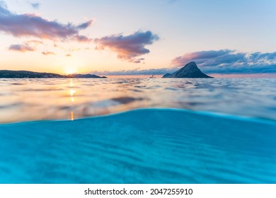 (Selective focus) Split-shot, over-under shot. Turquoise water in the foreground with Tavolara Island on the water surface during a stunning sunrise. Porto Taverna, Sardinia, Italy.