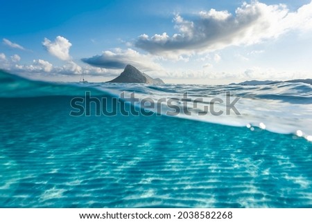 (Selective focus) Split-shot, over-under shot. Defocused turquoise water in the foreground with Tavolara island on the water surface during a sunny day. Porto Taverna, Sardinia, Italy.