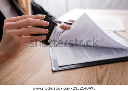 selective focus of stamper in hand of cropped notary near blurred contract