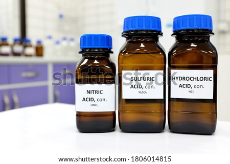 Selective focus of strong Nitric, Sulfuric and Hydrochloric acids in brown amber bottle. Blur white laboratory backdrop with copy space.