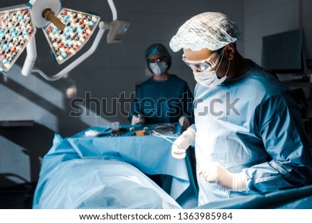selective focus of surgeon in uniform and medical cap doing operation 