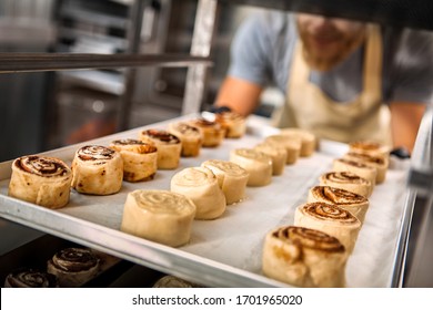 Selective focus of sweet cinnamon rolls at tray against bakery shop kitchen on blurred background with cropped view of young adult working man - Powered by Shutterstock