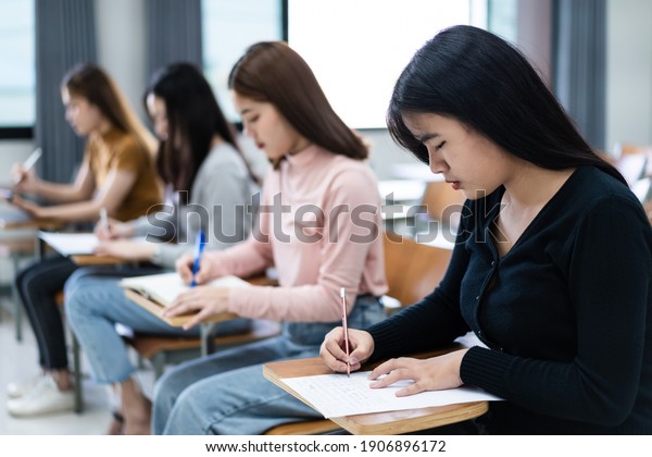 Selective focus of the teen college students\
sitting on lecture chair in classroom write on examination paper\
answer sheet in doing the final examination test. Female students\
in the student\
uniform.