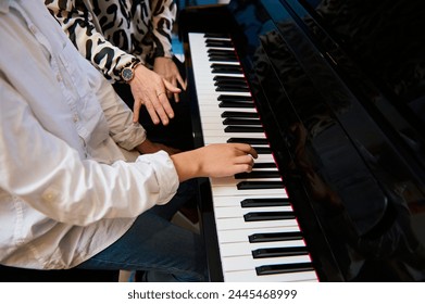 Selective focus to teenage boy musician pianist fingers and piano key to play the piano. Close-up child playing the piano during individual music lesson under his teacher's guidance. Musical education