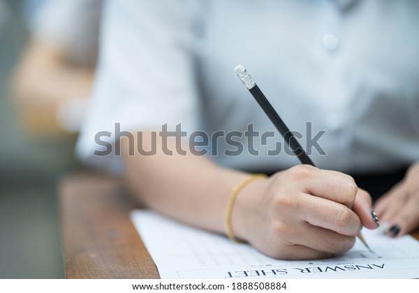 Selective focus of the teenage college\
students sit on lecture chairs do final examination and write on\
examination paper answer sheets in the classroom. University\
students in uniform in\
classroom.