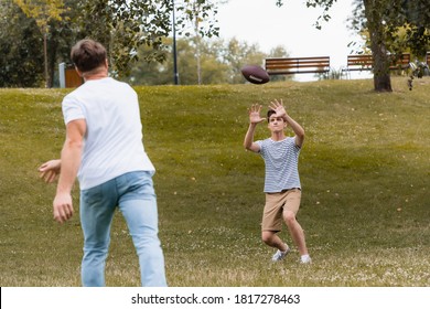 selective focus of teenager boy catching rugby ball near father in park - Powered by Shutterstock