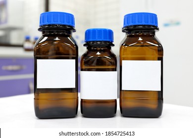 Selective Focus Of Three Dark Glass Reagent Bottle With Unknown Clear Liquid Chemical Inside And Blank Label In A Chemistry Laboratory.