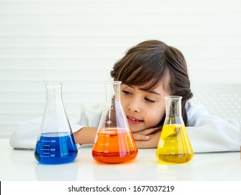 Selective focus, three flasks filled with blue, orange and yellow liquid with blurry background of cute girl looking at them. Science class