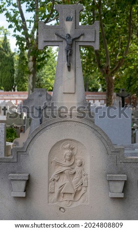 selective focus of a tombstone of a Catholic burial with a cross and a bronze sculpture of Christ and a relief of the Virgin of Carmen worn by time under the shade of some trees