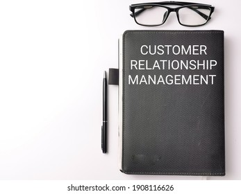 Selective focus top view text CUSTOMER RELATIONSHIP MANAGEMENT on black book with pen and eye glasses isolated on white background. Business concept.