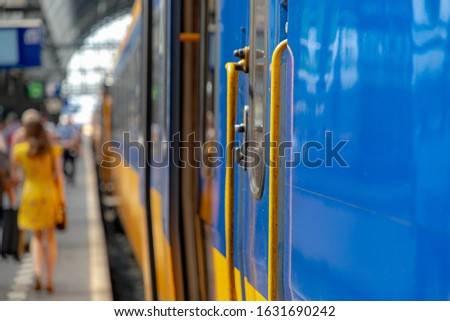 Selective focus of the train with blurred people traveling as background, Yellow blue bogie and passenger getting in and out the train in public station, Netherlands.
