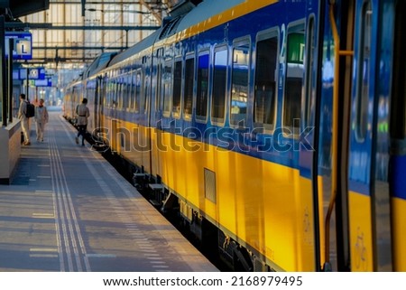 Selective focus of the train with blurred people traveling as background, Yellow blue bogie and passenger getting in and out the train in public station, Netherlands.