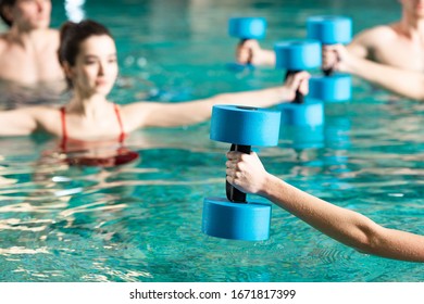 Selective focus of trainer with barbell working out with people in swimming pool